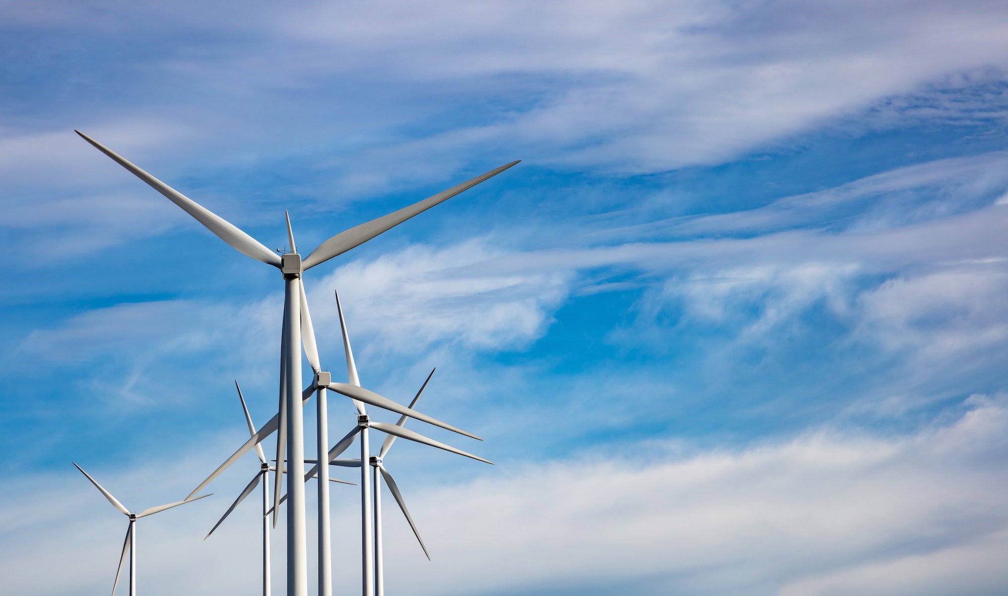 Tops of wind turbines against background of blue sky with wispy clouds